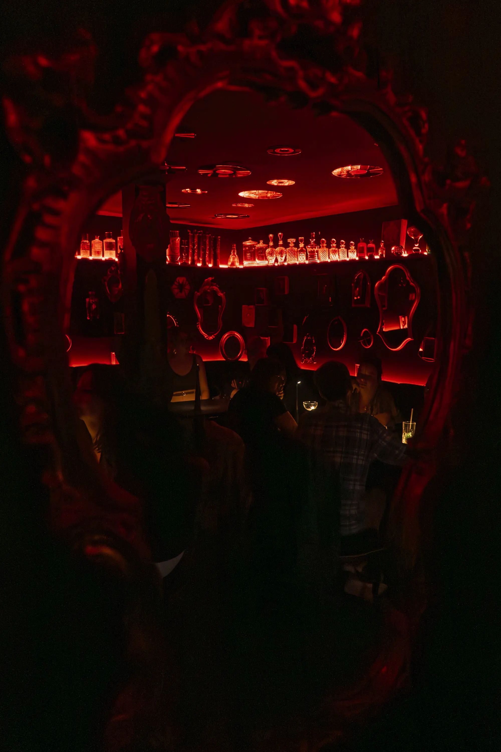 La Crypte vue à travers un miroir baroque : bouteilles rétro-éclairées et clients sous la lumière rouge