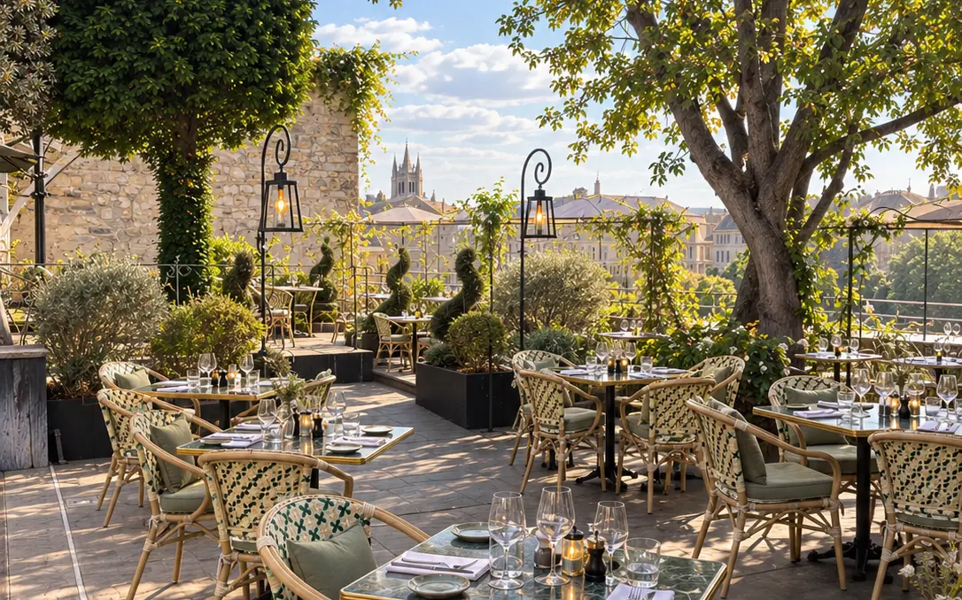 Le rooftop de L'Arche : tables dressées sous les arbres, lanternes en fer forgé et les toits d'Angers en arrière-plan